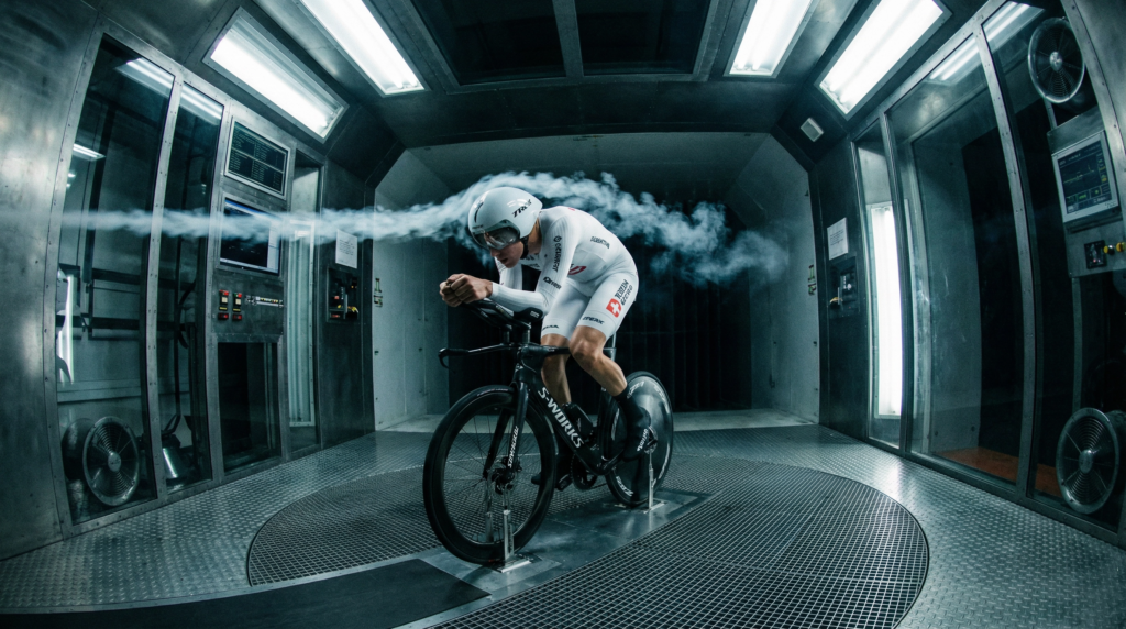 Professional cyclist in a white aerodynamic skinsuit being tested inside a modern wind tunnel facility