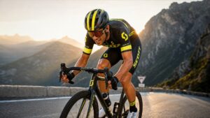 Professional road cyclist climbing mountain road in aerodynamic cycling apparel during sunset training ride