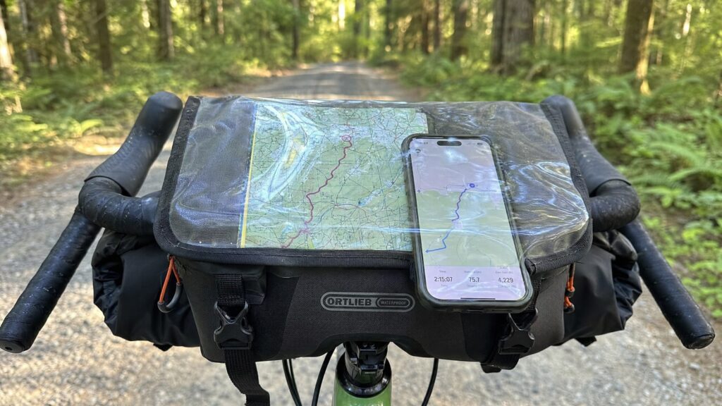 Waterproof handlebar bag mounted on a gravel bike handlebar with a smartphone showing a route
