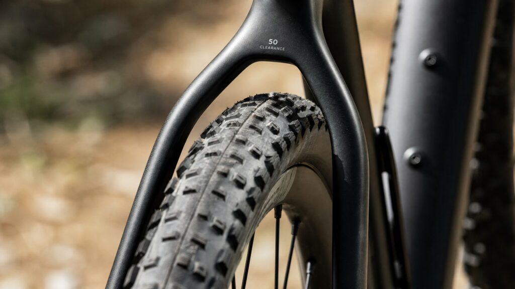 Gravel bike rear triangle showing a wide 50mm knobby tire with generous mud clearance on a matte carbon frame
