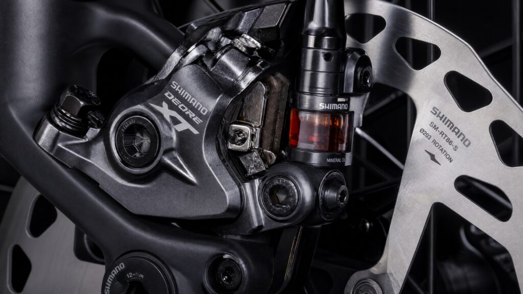 Shimano hydraulic disc brake caliper and large 203mm rotor showing the brake pads and fluid reservoir