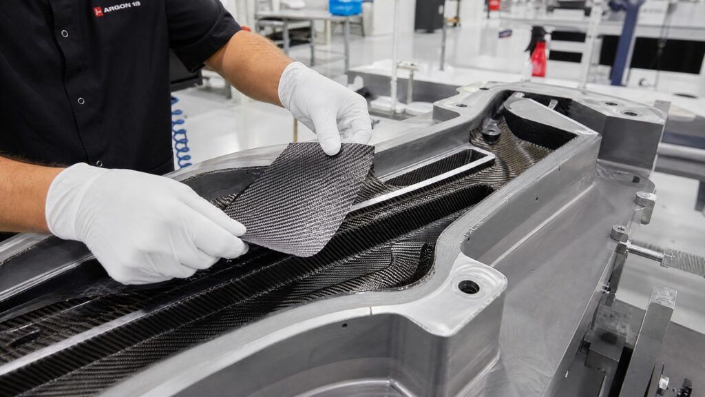 Technician laying pre-preg carbon fiber sheets into an open bike frame mold in a clean manufacturing facility